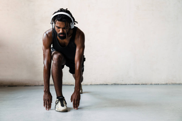 Image of athletic african american sportsman in headphones doing exercise while working out indoors - Foto, immagini