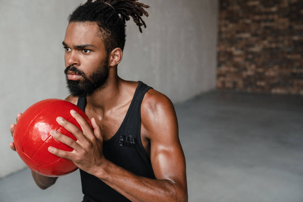 Image of athletic african american sportsman working out with medicine ball indoors - Valokuva, kuva