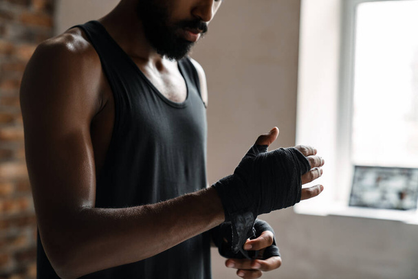 Image of athletic african american sportsman boxing in hand bandage while working out indoors - Фото, изображение