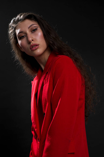 A young beautiful oriental woman with long black hair in a red jacket against a black background. The fashion model poses in the studio. - Φωτογραφία, εικόνα