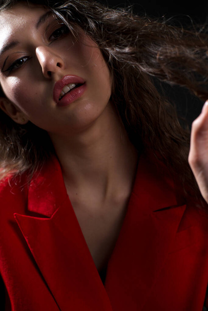 A young beautiful oriental woman with long black hair in a red jacket against a black background. The fashion model poses in the studio. - Fotoğraf, Görsel