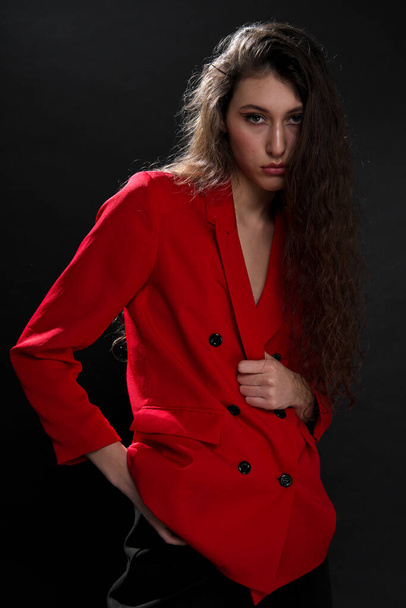A young beautiful oriental woman with long black hair in a red jacket against a black background. The fashion model poses in the studio. - Foto, Bild