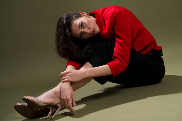 A sensual young woman in a red jacket, culottes and shoes with wet long black hair poses against a green background in the studio. - Foto, immagini