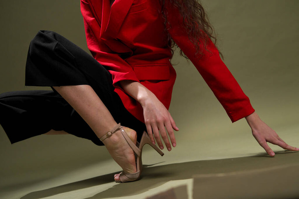 A sensual young woman in a red jacket, culottes and shoes with wet long black hair poses against a green background in the studio. - Фото, зображення