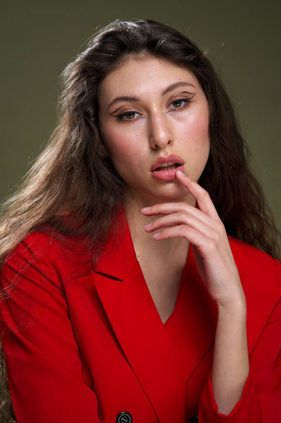 A sensual young woman portrait in a red jacket, with wet long black hair poses against a green background in the studio. - Photo, image