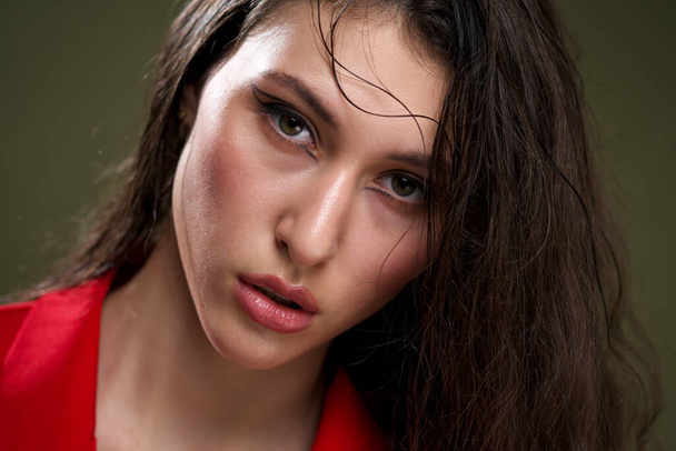 A sensual young woman portrait in a red jacket, with wet long black hair poses against a green background in the studio. - Foto, Bild
