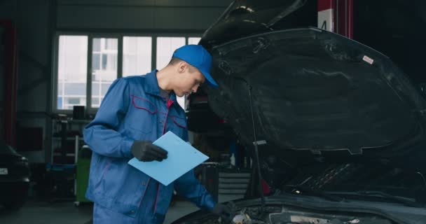 自動車保険の概念。機械検査官は、車両の損傷を調査し、サービスでメモ帳に書き込みます - 映像、動画
