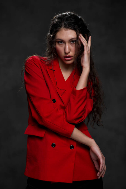 A young beautiful oriental woman with long black hair in a red jacket against a black background. The fashion model poses in the studio. - 写真・画像