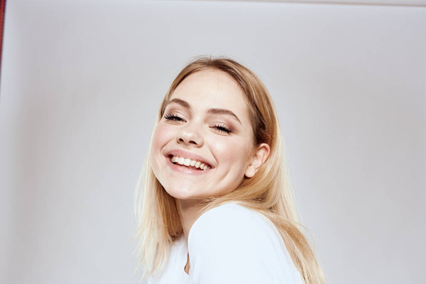 cheerful blonde in a white t-shirt gesturing with her hands light background - Fotoğraf, Görsel