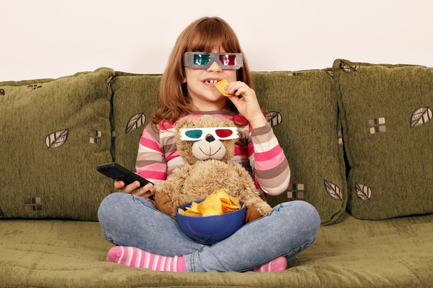 маленькая девочка с 3D очки едят чипсы и смотреть телевизор
 - Фото, изображение