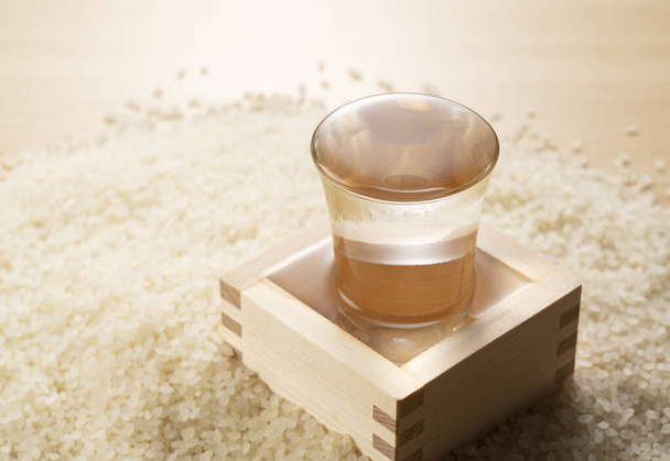 Verser le saké dans un verre de saké. Riz en arrière-plan. - Photo, image