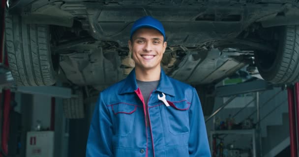 Portrait de beau mécanicien professionnel gestuelle OK et souriant à la caméra, debout à l'atelier de réparation automobile - Séquence, vidéo