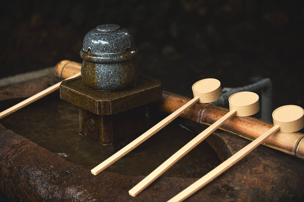 Mestolo di legno Posizionato su un bastone di bambù su un bacino di pietra, Chozuya usò l'acqua per lavarsi le mani prima di entrare in un tempio shintoista in Giappone. Posizionato nella zona d'ingresso, un look vintage dal tono scuro. - Foto, immagini