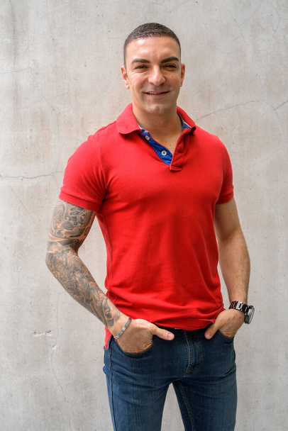 Счастливый красивый мужчина с татуировками, улыбающийся о бетонную стену - Фото, изображение