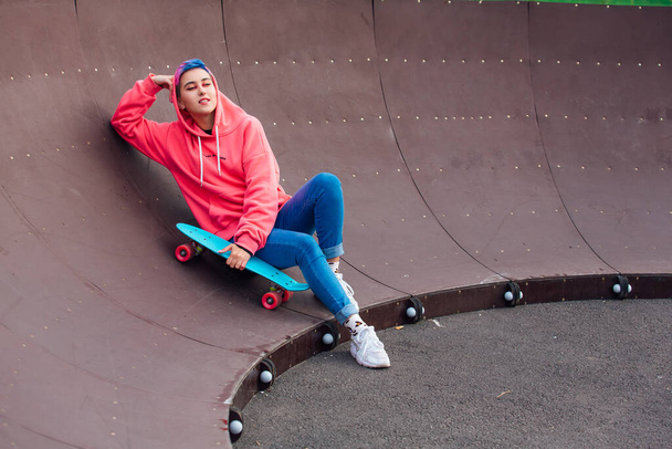Stylish young woman with short colored hair laying with her blue plastic skateboard in skatepark. Youth concept. - Fotografie, Obrázek