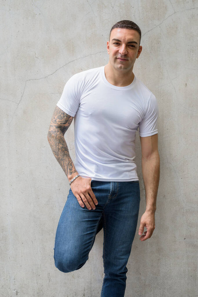 Portrait of handsome man with tattoos leaning against wall - Photo, Image