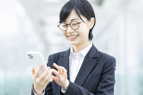 Asiatique jeune femme en costume et lunettes opérant un smartphone - Photo, image