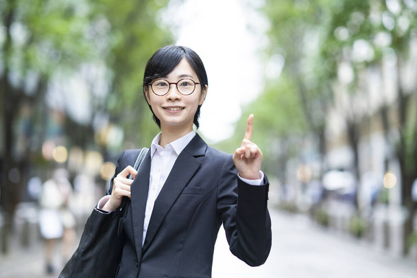 Eine junge Frau im Anzug posiert mit erhobenem Zeigefinger - Foto, Bild