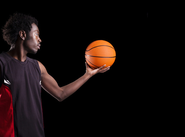 Portrait of a basketball player holding a ball against dark back - Фото, изображение