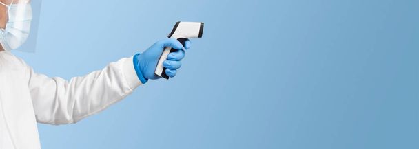 The doctor is measuring temperature with an white infrared thermometer on a blue color background , Coronavirus (COVID-19) prevention concept - Foto, Imagem