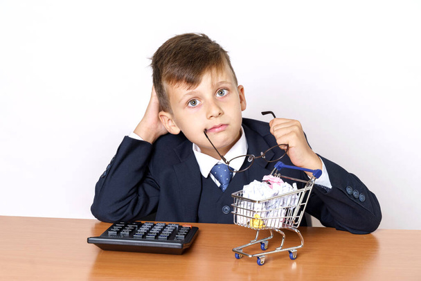 Business and finance concept. A young businessman is counting on a calculator, a mini shopping cart stands nearby. - Foto, imagen