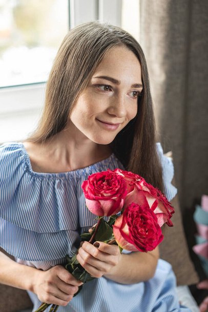 Ευτυχισμένη νεαρή γυναίκα με ένα όμορφο μπουκέτο από φρέσκα τριαντάφυλλα στο σπίτι. Έννοια των διακοπών, ειδύλλιο, καλή διάθεση. - Φωτογραφία, εικόνα