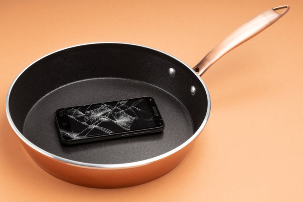 teléfono inteligente roto en una sartén negra, fondo naranja - Foto, Imagen