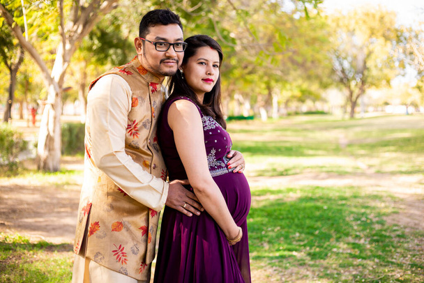 Fiatal ázsiai indiai terhes nő férjével visel hagyományos ruhát áll a parkban vagy kertben másolja helyet írni szöveg. - Fotó, kép