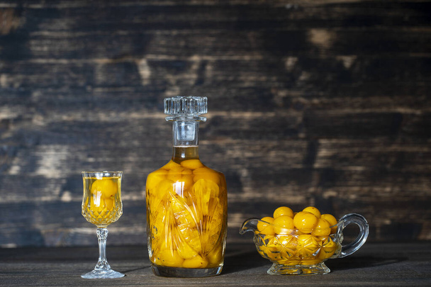 Homemade tincture of yellow cherry plum in a crystal bottle and a wine crystal glass on wooden background, Ukraine, close up. Berry alcoholic drinks concept - Zdjęcie, obraz