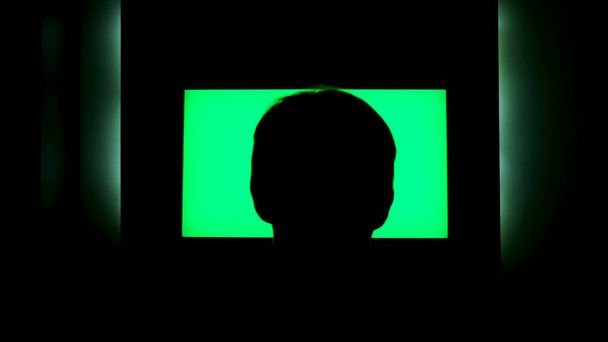緑の画面でテレビの前で男性の頭のシルエットのリアビュー。コンセプト。男見ますテレビとともにchromakeyそのハングオンザwll夜に自宅で. - 写真・画像