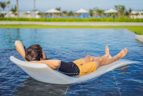 Relax in the pool. Young and successful man lying on a sun lounger and tans in the pool at the hotel - Photo, Image