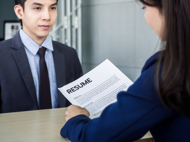Resume or CV paper in employer 's hand and review the applicant profile. Asian businesswoman, HR reading resume of young Asian man in suit in office. Job interview and employment concept. - Photo, Image