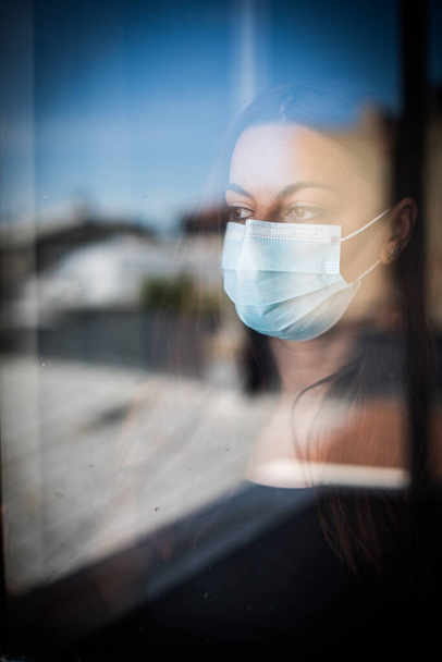 Immagine a colori di una donna che indossa una maschera chirurgica vicino a una finestra. - Foto, immagini
