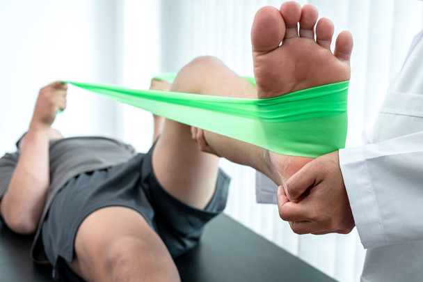 Физиотерапевт работает над обследованием травмированной ноги пациента спортсмена, врач проводит восстановительную терапию боли в клинике. - Фото, изображение