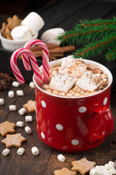 マシュマロとホットチョコレートドリンクの大きな赤いカップ,ジンジャーブレッドクッキー,暗い木製の背景にキャンディー杖とシナモン.冬時間だ。休日の概念、選択的焦点 - 写真・画像