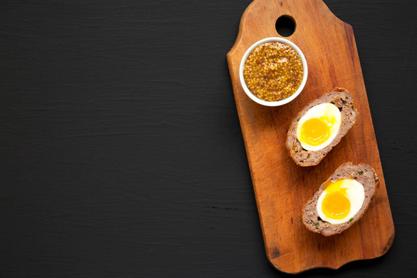 Homemade Scotch Eggs on a rustic wooden board on a black background, top view. Flat lay, overhead, from above. Copy space. - Photo, Image