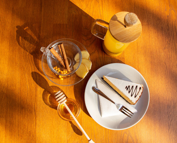 vörhenyes tengeri homoktövis tea fahéjas botokkal és egy darab frissen sült torta egy fából készült asztalon - Fotó, kép