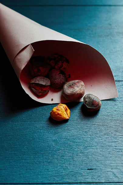roasted chestnuts in a paper over a blue wood table - Photo, Image