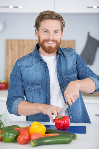 smiling young man chopping vegetables in the home - 写真・画像