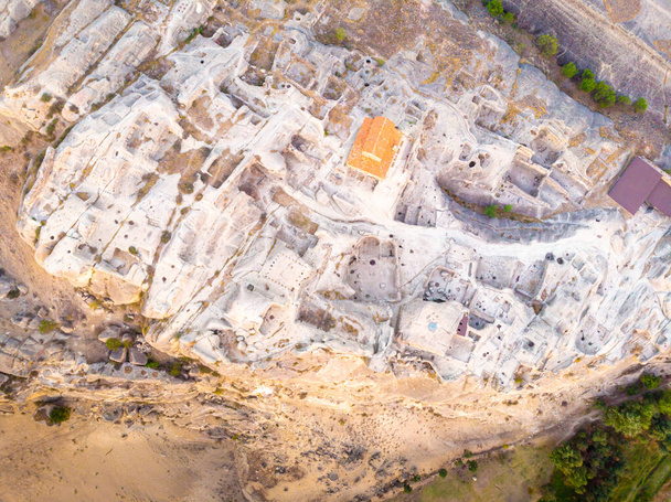 Madarak szem előtt le struktúrák és barlangok labirintus Uplistsiche barlang város bazilika narancs tetővel. Utazás és történelmi helyek Grúziában. - Fotó, kép