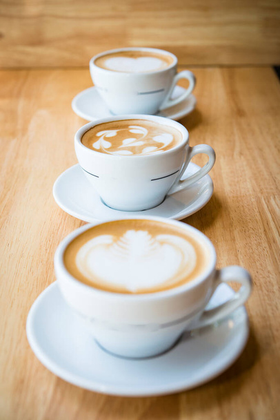 Drie kopjes hete cappuccino koffie met hart koffie rt op de top met melk - Foto, afbeelding
