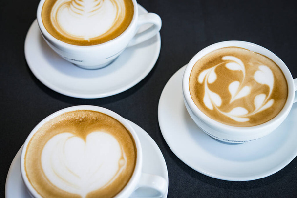 3カップのホットカプチーノコーヒーとハートコーヒーアートの上にミルク - 写真・画像