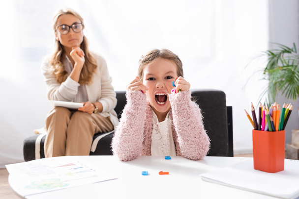 little girl patient screaming and clenching figures while visiting psychologist - Photo, image
