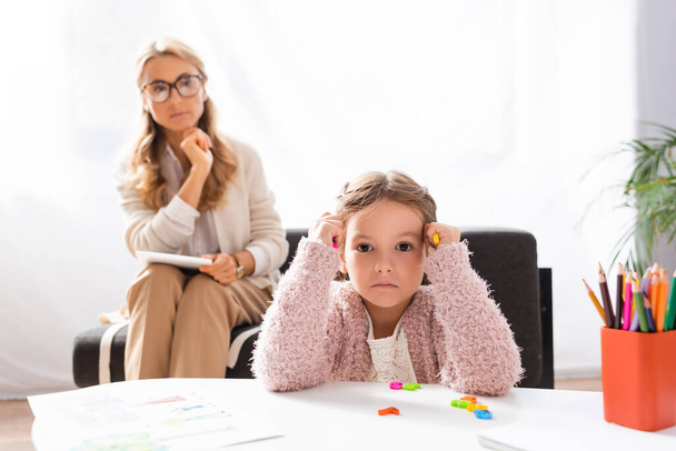 little girl looking at camera and holding colorful figures while visiting psychologist - Photo, image