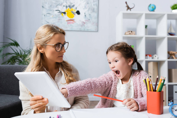 małe dziecko krzyczące i wskazujące na cyfrową tabletkę podczas wizyty u psychologa - Zdjęcie, obraz