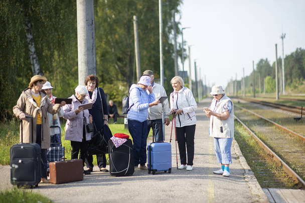 Skupina pozitivních seniorů, kteří cestují s tabletami a čekají na vlak. - Fotografie, Obrázek