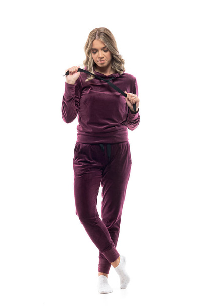 Cute young thoughtful woman relaxing at home getting dressed in comfy tracksuit and socks. Full body isolated on white background. - Photo, Image