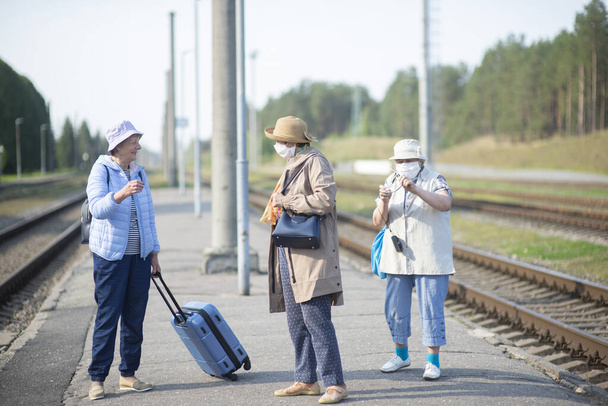 Tres ancianas en la plataforma esperan el tren y llevan una máscara facial durante una pandemia - Foto, Imagen