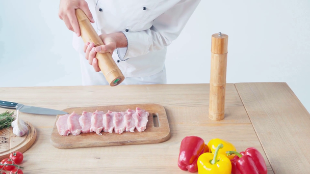 Vista ritagliata dello chef con macinino condimento crudo pezzi di maiale su bianco - Filmati, video
