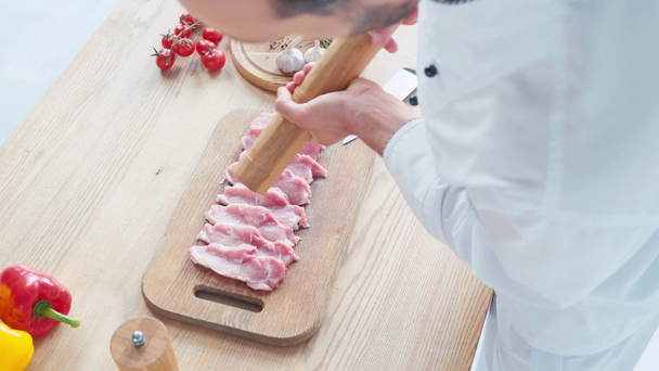 Vista de alto ángulo del chef con sazonador molino rodajas crudas de cerdo en la mesa - Metraje, vídeo